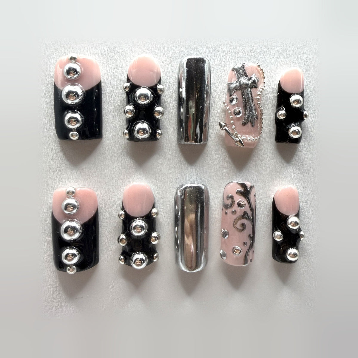 Grunge Girl press-on nails: ten medium square black and blush-pink nails with raised silver studs, mirror-chrome accents, a sculpted silver cross and silver scrollwork