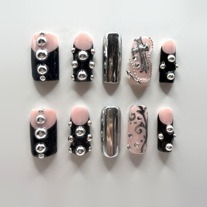 Grunge Girl press-on nails: ten medium square black and blush-pink nails with raised silver studs, mirror-chrome accents, a sculpted silver cross and silver scrollwork